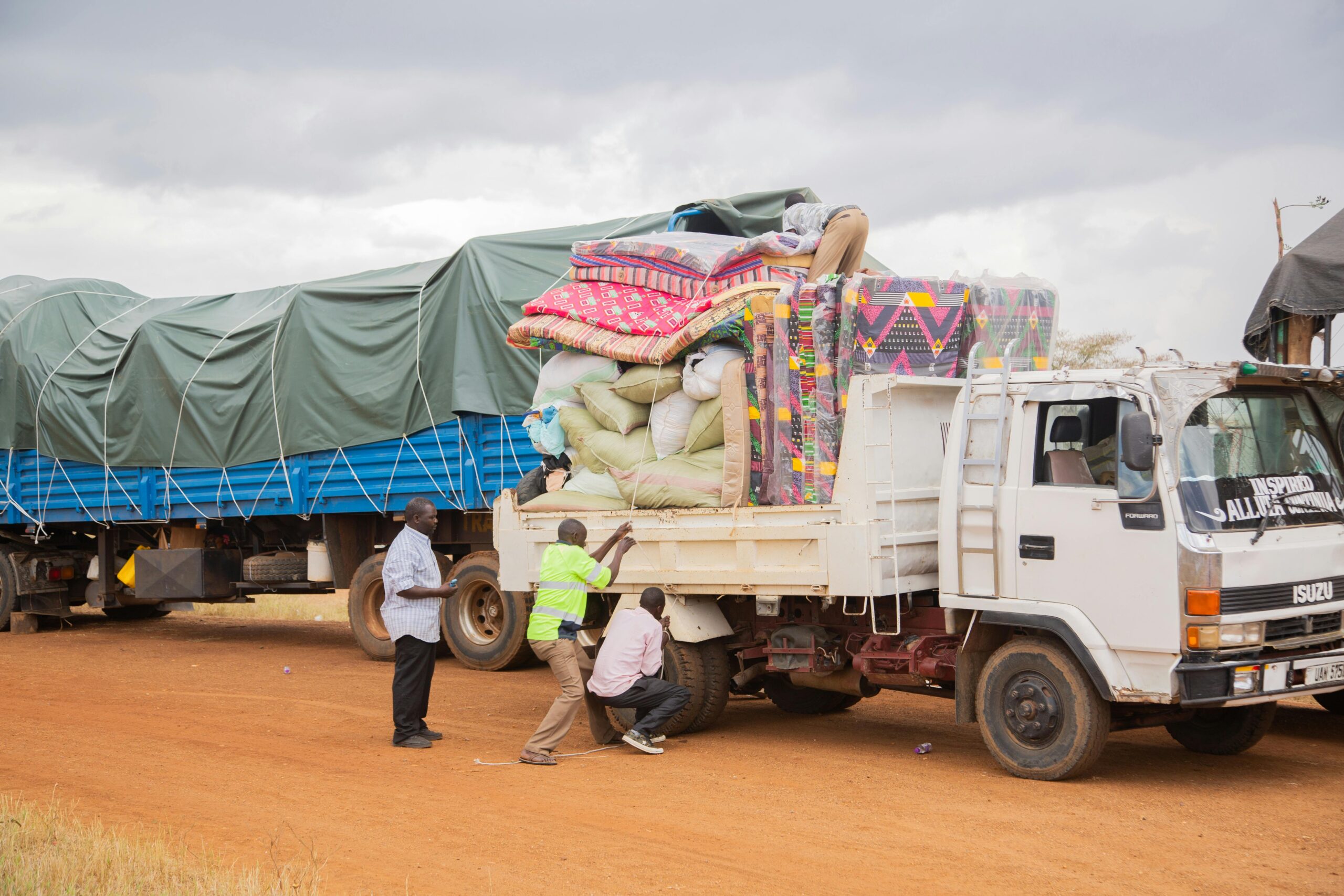 People loading supplies onto a truck in a rural area under cloudy skies.
